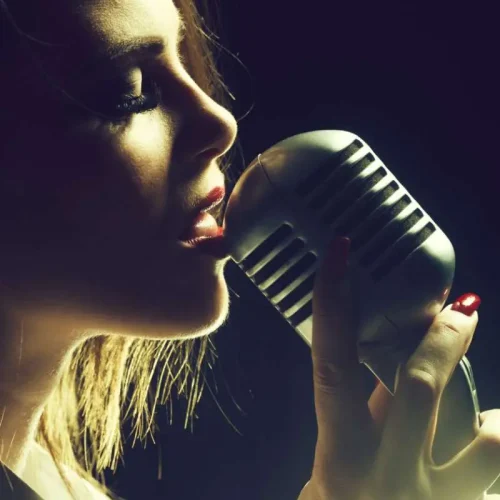 young sexy woman profile with pretty face and red lips singing into studio silver microphone with long hair, closeup